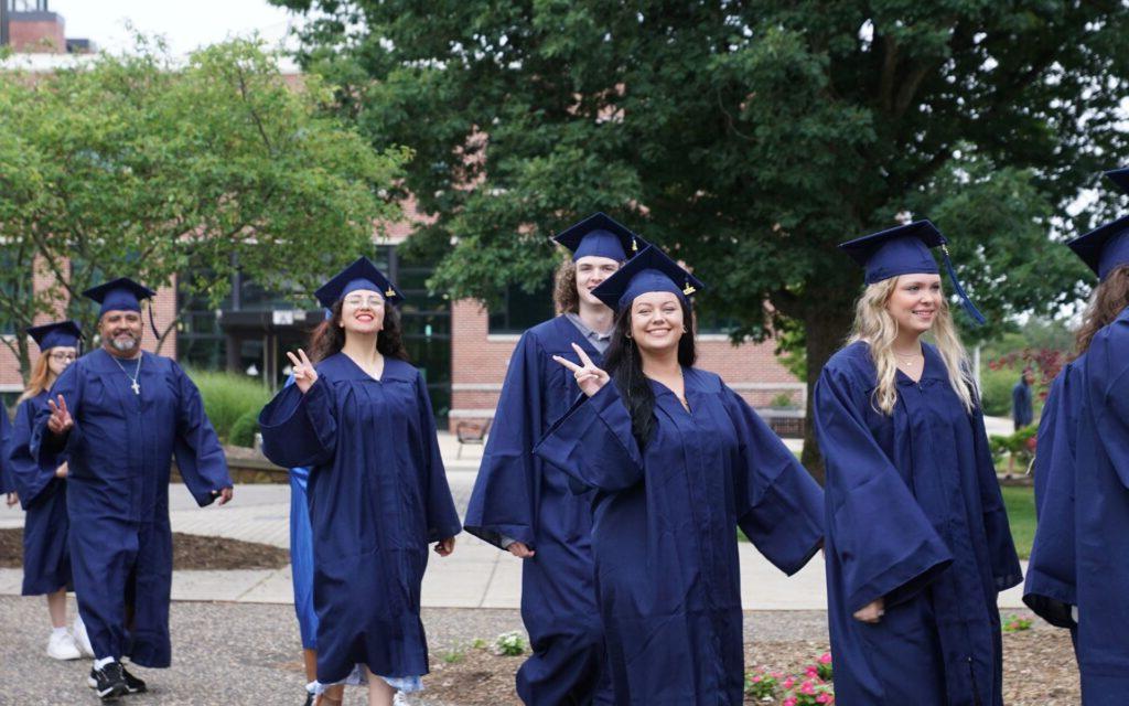 Students at graduation smiling at the camera and showing peace signs with their hands.