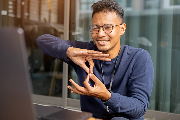 A man using sign language to communicate with colleagues via laptop.